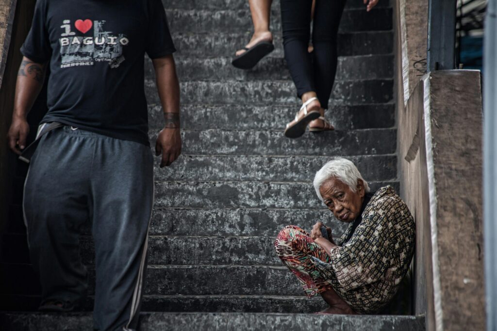 An elderly person sitting on a staircase in an urban environment. Filipino cityscape.