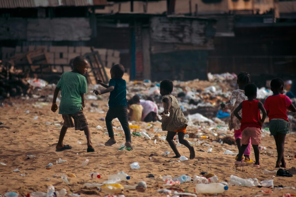 Children play on a waste-covered urban beach, highlighting pollution and climate challenges.